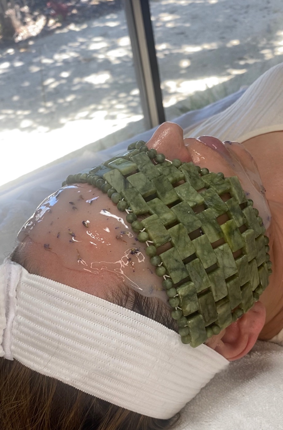 Client relaxing with a jade facial roller mask during a treatment